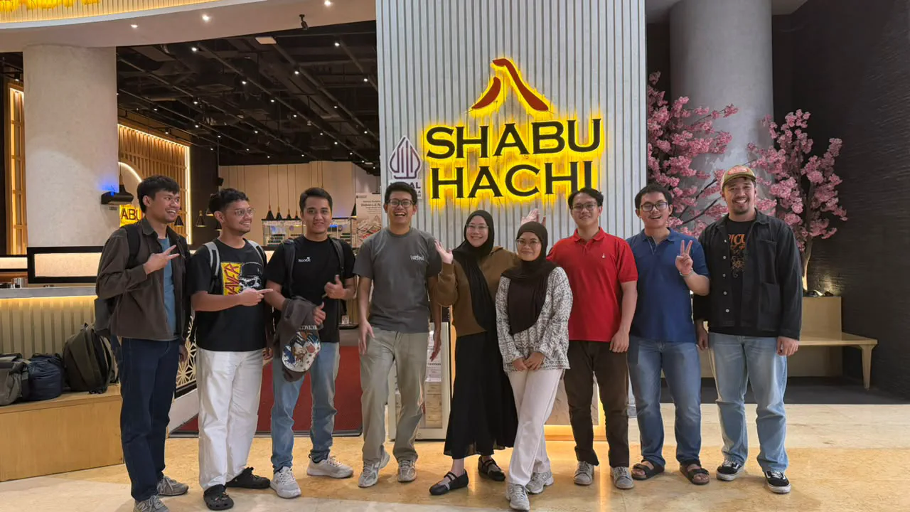 Nine people posing in front of the Shabu Hachi restaurant sign in a mall.
